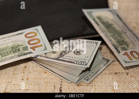 Stack of Hundred Dollar Bills Partially in a Black Wallet on a Table Stock Photo