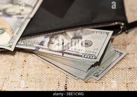 Stack of Hundred Dollar Bills Partially in a Black Wallet on a Table Stock Photo
