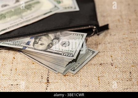 Stack of Hundred Dollar Bills Partially in a Black Wallet on a Table Stock Photo