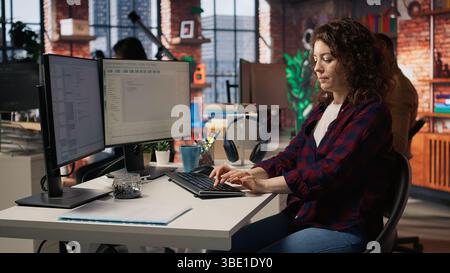 Happy employee using programming languages on PC in IT startup office to build applications. Cheerful IT expert using computer in software development agency to code, camera A Stock Photo