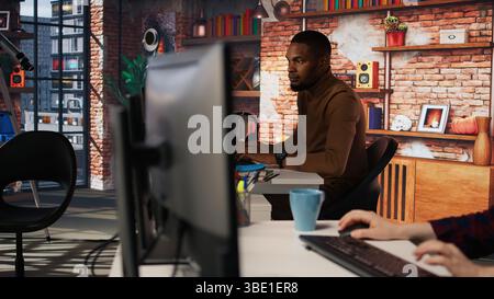 Irked man punching startup office desk in frustration struggling to fix application errors. Upset programmer annoyed by computer bugs while coding in software development agency, camera A Stock Photo