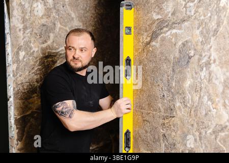 Builder checking the evenness of marble tiles with a level tool, ensuring precision and accuracy during renovation work on a wall Stock Photo
