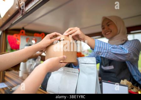 Chinese muslim female in hijab barista serving drinks and snacks to customers. A small business of a coffee shop or cafe on a truck Stock Photo