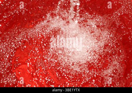 A close-up view of water being poured into a red bucket. The turbulence and bubbles created by the water stream are vividly highlighted. Stock Photo