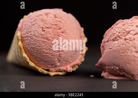 melting pink ice cream on a black slate board, sweet cold pink ice cream with strawberry flavor, ice cream in a waffle cone, close up Stock Photo