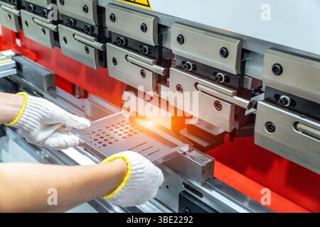 The technician operator working with sheet metal on CNC hydraulic press brake. He puts the part and bends it into a large machine at an angle. Stock Photo