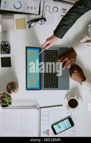 Two individuals working together on business project with laptop, documents, and smartphone arranged on desk. Scene captures productive workplace envi Stock Photo