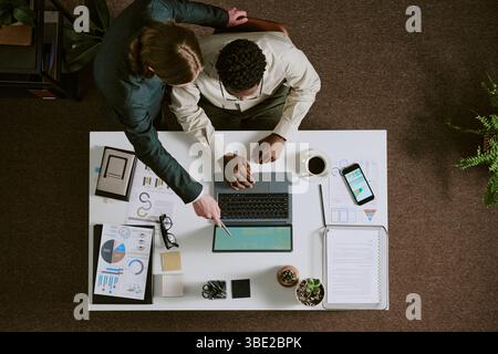 Overhead view of two colleagues working together on project, utilizing laptop, tablet, and documents on desk, exchanging ideas and discussing strategi Stock Photo