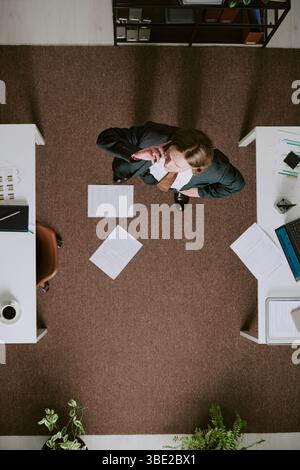 Businessman standing in office, surrounded by scattered documents on floor while contemplating something important with items like keyboard and plants Stock Photo