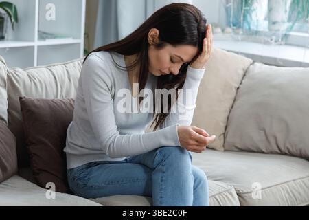 Young woman suffering from headache sitting on couch at home Stock Photo