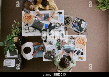 Group of professionals working on modern technology solutions in collaborative office setting, with visible gadgets and equipment around. Top-down vie Stock Photo