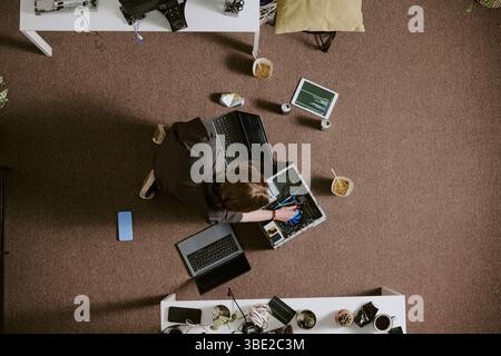 Overhead view of man working on repairing laptop motherboard at his desk surrounded by various tools and gadgets Stock Photo