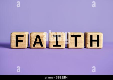 Wooden blocks spelling the word FAITH on purple background. Belief concept Stock Photo