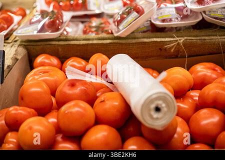 ripe farm tomatoes in a container with a roll of disposable bags in a supermarket Stock Photo