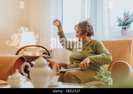 Elderly Woman Knitting in a Cozy Room Filled with Warm Natural Light Stock Photo