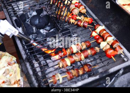 Large metal grill fired with a gas burner. Grilled cheese and colorful skewers being grilling on the rack Stock Photo