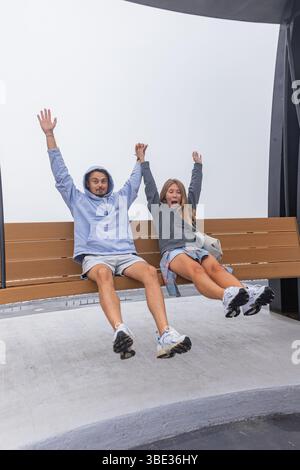 Young couple swinging playfully on large modern bench outdoors Stock Photo