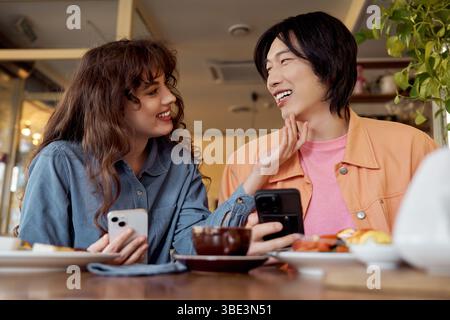 A young multicultural couple enjoys a light-hearted conversation over coffee at a cafe. Stock Photo
