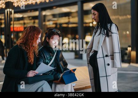 Three colleagues collaborating outside on documents and tablet with trendy clothing Stock Photo
