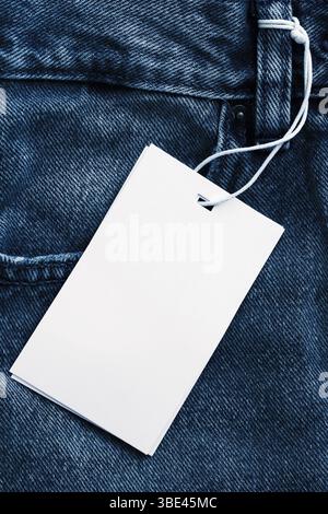 Blank white label on denim jeans. Price tag with string. Close-up of clothing detail. Fashion branding concept. Shopping, sale, and garment label. Stock Photo