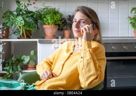 Assured woman speak on call amidst houseplants, offer advice from home office. Online consultation Stock Photo