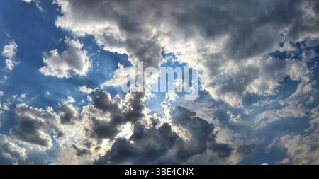 A panoramic view of a dynamic cloudy sky with sunlight streaming through gaps in the clouds, creating a dramatic and serene atmosphere that captures t Stock Photo