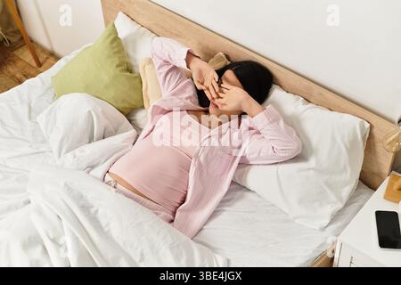 A young woman relaxes in bed, hands over her eyes, enjoying the morning calm. Stock Photo