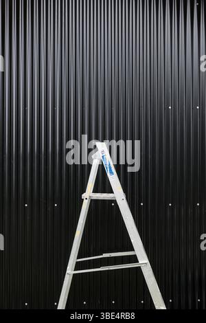 An aluminium stepladder in front of a new black corrugated iron wall Stock Photo