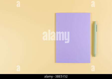 Top view of purple notebook, green pen on yellow background. School, office wallpaper. Flat lay, copy space. Stock Photo