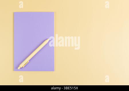 Top view of purple notebook, yellow pen on yellow background. School, office wallpaper. Flat lay, copy space. Stock Photo