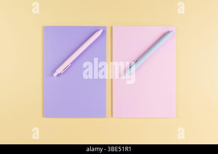 Top view of pink and purple notebooks, pink and blue pens on yellow background. School, office wallpaper. Flat lay, copy space. Stock Photo