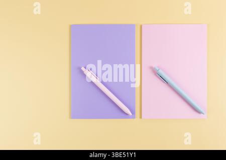 Top view of pink and purple notebooks, pink and blue pens on yellow background. School, office wallpaper. Flat lay, copy space. Stock Photo