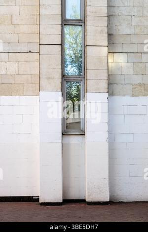 brick wall of city house painted white from below with narrow window on spring day Stock Photo