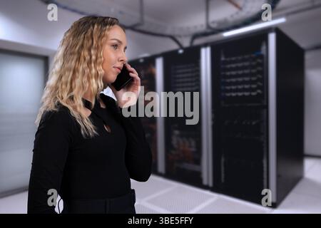 Woman on a phone call in data center with server racks behind Stock Photo