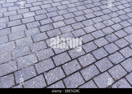 a gray paving stone consisting of rectangular stone blocks arranged in regular rows in a diagonal pattern. Stock Photo