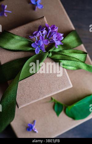 A beautifully wrapped gift box adorned with a vibrant green ribbon and delicate purple flowers. The arrangement is perfect for celebrating special occ Stock Photo