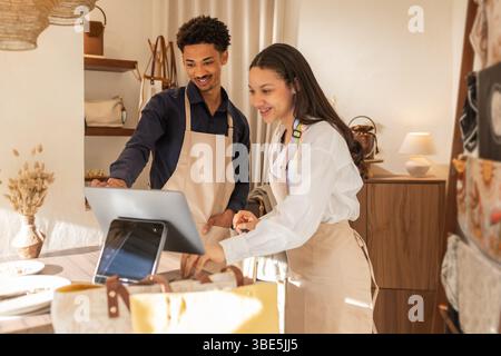 Two cheerful employees in a bag store using a tablet for checkout. They're standing behind the counter, surrounded by various bags and accessories on Stock Photo