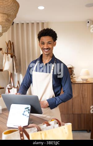 Smiling shop assistant in a bag store using a digital tablet to assist customers. Surrounded by various handbags, creating a welcoming and modern reta Stock Photo