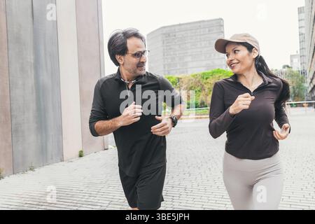 A joyful couple is jogging together on a city street, dressed in sportswear. They enjoy the refreshing morning air as they maintain a healthy lifestyl Stock Photo