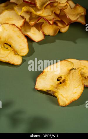 A close-up image showcasing crispy, dried apple slices elegantly arranged on a smooth green surface. Stock Photo