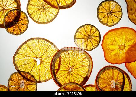 A vibrant display of translucent slices of various dried fruits illuminated from behind. Visible are dried oranges, apples, and persimmons, showcasing Stock Photo