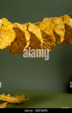 A close-up shot of beautifully dried pineapple slices arranged in a row against a muted green backdrop, showcasing the texture and rich yellow hues of Stock Photo