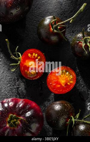 A close up of various black and red cherry tomatoes with water droplets on a dark slate surface, highlighting their fresh and vibrant textures. Stock Photo