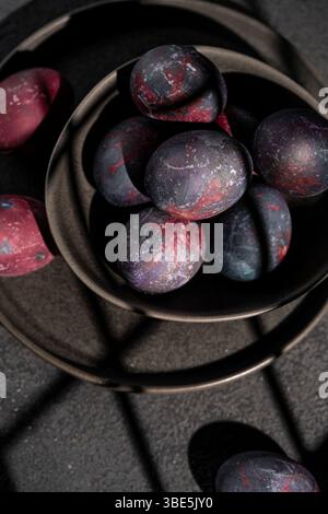 Top view of a ceramic bowl filled with dark, galaxy themed Easter eggs against dark background surface Stock Photo