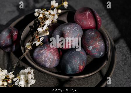 A moody and captivating arrangement featuring dark, galaxy-themed Easter eggs lying in a rustic bowl, accentuated by delicate white spring blossoms. Stock Photo