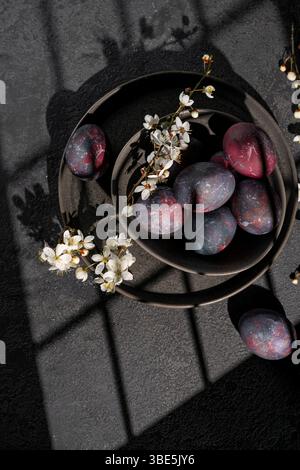 Top view of artistically painted dark Easter eggs nestled among delicate white spring blossoms on a textured black background. Stock Photo