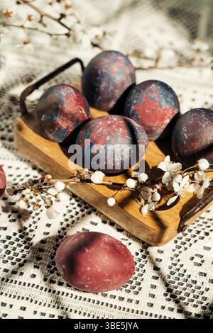 A rustic display of colorful, artistic Easter eggs nestled in a wooden tray adorned with delicate spring blossoms against crochet tablecloth Stock Photo