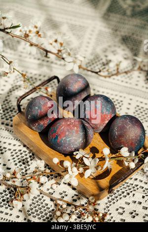 Artistic Easter eggs with a unique galaxy pattern displayed on a wooden tray, adorned with blooming spring branches, set on a crochet tablecloth texti Stock Photo