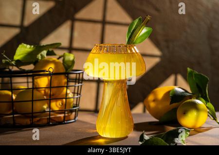 A vibrant lemon drink served in a unique glass with a straw, set against a rustic background. Fresh lemons in a basket add a natural touch to this ref Stock Photo