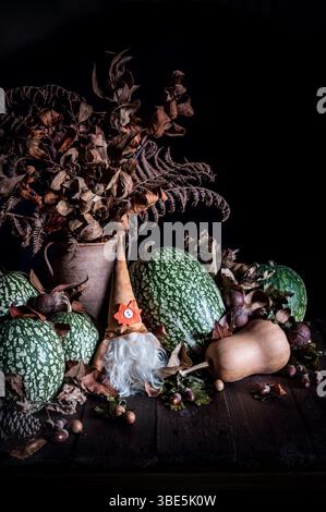Autumn scene with green pumpkins, dried leaves, and a gnome statue on a rustic wooden table. The arrangement evokes the cozy and earthy essence of the Stock Photo